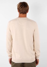 Pull en maille beige avec des manches longues, un col rond et des poignets côtelés. Il présente une texture lisse et un design simple et classique.