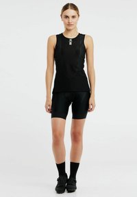 Zwarte sportieve tanktop met netpanelen en een slank ontwerp, gecombineerd met strakke zwarte fietsbroeken en zwarte sportschoenen.
