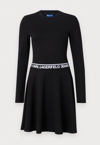Black long-sleeve dress made of stretch fabric, featuring a fitted bodice, flared skirt, and a white branded elastic waistband.