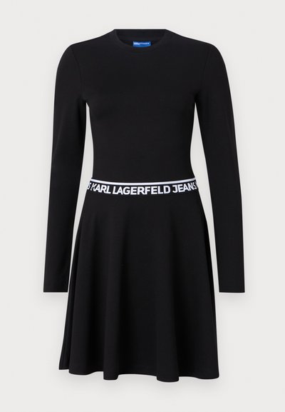 Robe noire à manches longues en tissu extensible, avec un corsage ajusté, une jupe évasée et une ceinture élastique blanche avec logo.