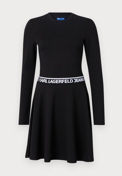 Robe noire à manches longues en tissu extensible, avec un corsage ajusté, une jupe évasée et une ceinture élastique blanche avec logo.