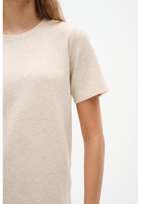 Beige tričko s krátkým rukávem vyrobené z jemné látky, s kulatým výstřihem a minimalistickým designem. Jemná textura bez viditelných vzorů.