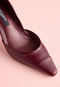 Bordové kožené lodičky so špicatou špičkou, hladkým povrchom, otvorenými stranami a mierne zdvihnutým podpätkom. Viditeľné sú len minimálne švy.