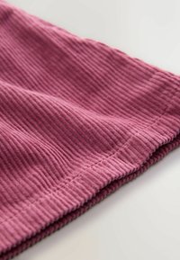 Tessuto testurizzato in rosa tenue con righe verticali. Il bordo presenta un delicato orlo cucito, che sottolinea il materiale morbido e flessibile.