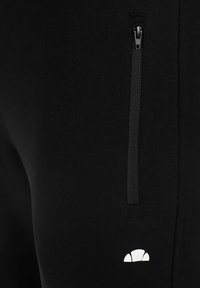 Close-up van zwart materiaal met een verticale ritszak en een klein wit halve cirkel logo nabij de onderrand.