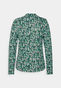 Chemise à manches longues en tissu vert avec un motif floral. Présente de petites fleurs blanches, roses et turquoise sur un fond sombre. Col arrondi.