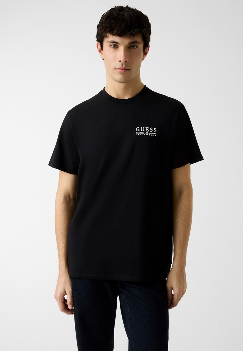 Schwarzes Baumwoll-T-Shirt mit einem weißen Logo auf der Vorderseite, kurzen Ärmeln, rundem Ausschnitt und lockerer Passform.