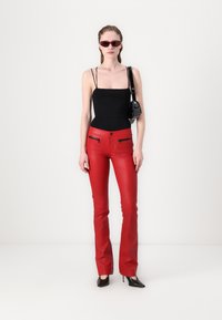Red leather flared pants with zippered pockets, paired with a black fitted tank top. Accessories include small black handbag and red-tinted sunglasses.