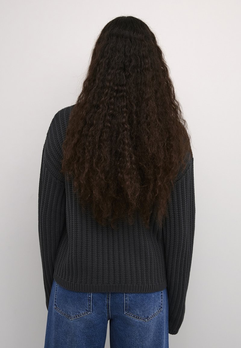 Ciemnoszary, textured sweter z dzianiny o prążkowanym wzorze i długich rękawach, zestawiony z niebieskimi dżinsami z wysokim stanem. Widok od tyłu.