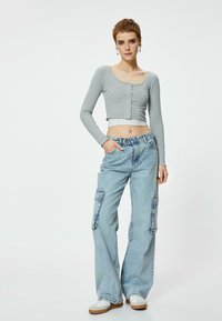 Top a maniche lunghe cropped rigato grigio chiaro con scollo rotondo e bottoni, abbinato a jeans cargo larghi blu chiaro con tasche laterali.