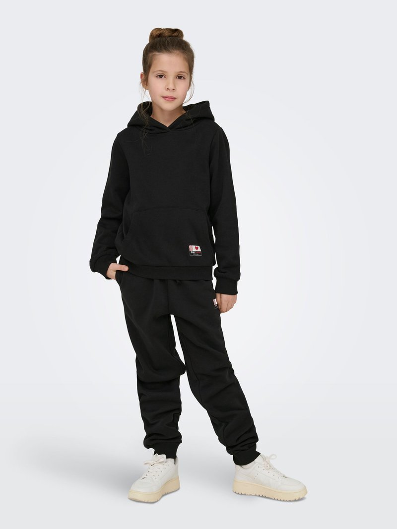 Melns kokvilnas sporta krekls ar priekšējo kabatu un auklām, kombinēts ar melnām sporta biksēm un baltiem sporta apaviem. Vienkāršs dizains, brīvs piegriezums.