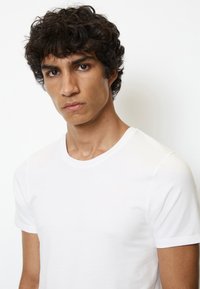 T-shirt bianco in cotone con scollatura rotonda, maniche corte e tessuto liscio, aderente al corpo. Design semplice e versatile.