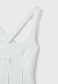 Robe blanche sans manches avec des bretelles épaisses qui se croisent dans le dos et des détails de coutures verticales sur le corsage.