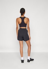 Svart idrotts crop top med racerback-design, matchad med mörka shorts. Modellen bär svarta skor och vita strumpor. Slät tygstruktur.