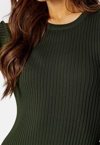 Haut en maille côtelée verte avec un col rond et une coupe ajustée, orné de rayures verticales texturées créant une apparence structurée.