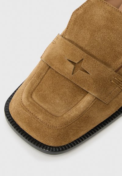 Chaussure slip-on en daim brun clair avec un bout arrondi, semelle en caoutchouc noir et une large bride avec un détail en forme d'étoile découpé.