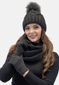 Caciula tricotată neagră cu pompom, mănuși asortate și o eșarfă groasă, având o textură cu diafragmă și un detaliu discret cu eticheta brandului.