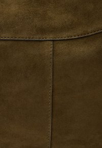 Borsa in suede di un verde oliva scuro con una texture liscia, cuciture a punto e un design flat. Presenta una chiusura a pattina e dettagli hardware minimali.