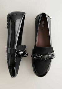 Sorte loafers med patentfinish og ruskindsdetaljer. Har en knyttet detalje på remmen, forhøjet sål og rund tå-design.