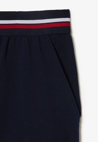 Pantaloni jogger in tessuto blu navy con una cintura elastica spessa caratterizzata da strisce rosse, bianche e blu; tasche laterali e una texture liscia.