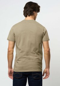 Khaki puuvillainen t-paita lyhyillä hihoilla, pyöreällä pääntiellä ja sileällä pinnalla, yhdistettynä tummiin farkkuihin, joissa on takataskut.