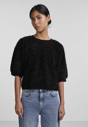 Pull en tricot noir pelucheux avec des manches courtes et oversize et un col rond côtelé. Porté avec un jean bleu taille haute.