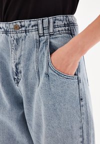 Světlé modré džíny z denimu s volnějším střihem, poutky na pásek, předními kapsami a kovovým knoflíkem na pásku. Texturovaná látka.