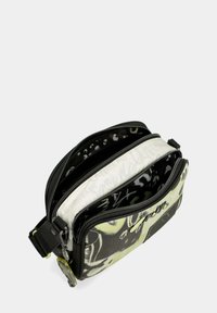 Bolso bandolera de patrón en blanco y negro con múltiples compartimentos con cremallera, que presenta una textura suave y un sutil detalle de logo.