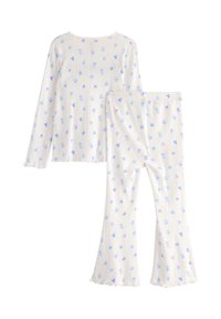 Ensemble de pyjama côtelé en blanc avec un motif floral bleu. Haut à manches longues avec un col rond ; pantalons évasés avec des ourlets à volants. Matière douce.