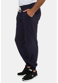 Marineblaue Jogginghose aus weichem Stoff, mit einem Kordelzugbund, zwei Seitentaschen und einem dezenten Logo am linken Bein.