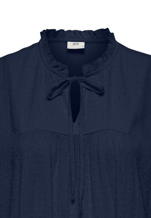 Blusa blu navy con un motivo testurizzato a pois. Presenta un collo arricciato e un dettaglio con fiocco nell'apertura a chiave.