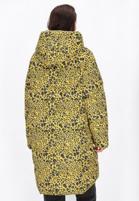 Gul puffjacka med svarta och blå leopardprickar, med huva, långa ärmar och en lös passform. Strukturerat tyg och vadderad design.