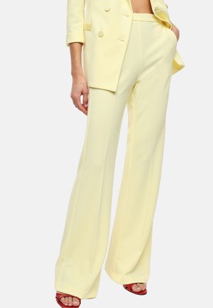Donna che indossa pantaloni a gamba larga giallo pallido a vita alta e blazer abbinato con maniche arrotolate, abbinati a tacchi aperti rossi.