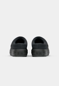 Sorte, polstrede slip-on sko med avrundte bakdeler og teksturerte gummisåler. Har preget merkevare på hælen og glatte sømdetaljer.