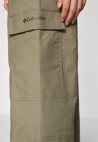 Olive-zeleno Columbia cargo hlače imajo teksturirano tkanino, vidne šive in logotipni našitek na sprednjem žepu, kar odraža praktično zasnovo.