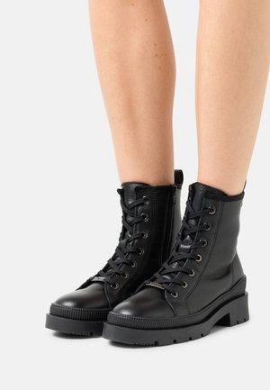 Black ankle boots made of leather with a round toe, lace-up front, textured surface, side zipper, and a chunky rubber sole.