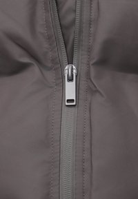 Sección de chaqueta gris con un cierre suave, tejido texturizado y costura reforzada a lo largo de la línea del cierre para mayor durabilidad.