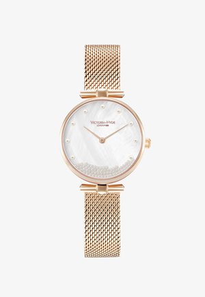 Montre ronde avec un bracelet en maille dorée rose, un cadran en nacre blanche et des perles décoratives. Elle présente des marqueurs d'heure minimalistes et un logo.