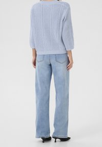Helle blaue Strickjacke mit strukturiertem Muster und Dreiviertelärmel, kombiniert mit hoch geschnittenen hellen Jeans und schwarzen High Heels.