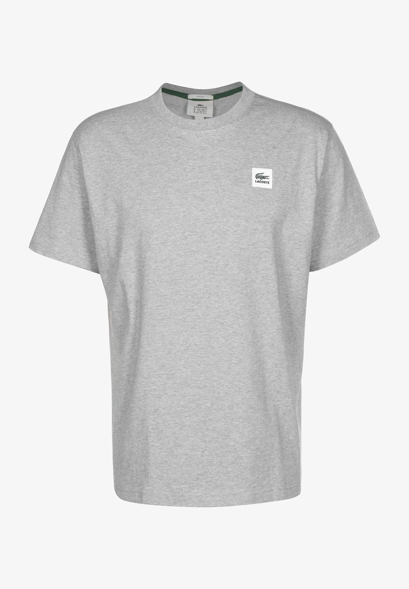 T-shirt gris clair à manches courtes avec col rond, petit écusson logo Lacoste sur la poitrine gauche et détail vert à l’intérieur du col.