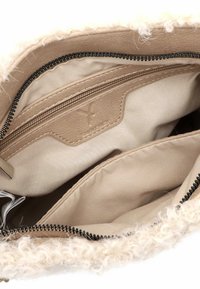Interno di una borsa beige con una fodera morbida e texturizzata. Presenta una tasca con zip e una sezione in pelle di colore marrone chiaro con un marchio in rilievo.
