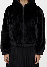 Black faux fur hoodie with a zip closure, elasticated waistband, and long sleeves, paired with a black pleated skirt. Soft texture and cozy design.