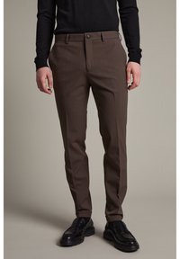 Bruna skräddarsydda byxor med rak benform, slät textur och en enkel knappstängning. Stylingen kompletteras med en svart långärmad stickad topp och svarta loafers.