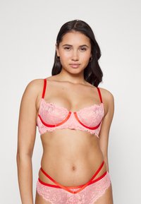 Sutiã de renda rosa com detalhes vermelhos, apresentando padrões florais e alças finas, desenhado com uma forma estruturada e bordas em forma de escalope.