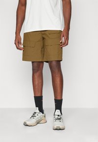 Olivengrønne cargo shorts i let stof, med to frontlommer, lige pasform og længde til midten af låret, parret med hvide sneakers.