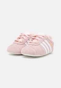 Par de zapatillas Adidas Gazelle para niños en rosa con rayas y cordones blancos sobre un fondo claro.