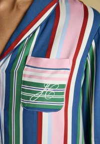 Striped pajama shirt with blue, green, pink, and red hues. Features a pocket with a multi-striped pattern and an embroidered initial. Soft fabric.