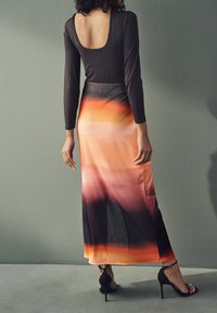 Haut noir à manches longues avec un dos en scoop associé à une jupe maxi dégradée orange à noir, dotée d'une texture lisse et d'une fente haute. Talons noirs.