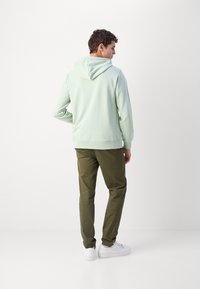 Felpa verde chiaro con vestibilità rilassata, cappuccio regolabile e polsini a coste. Abbinate a pantaloni verde oliva e sneaker bianchi.