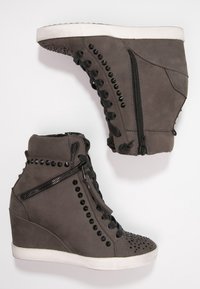 Sneakers na koturnie z szarego zamszu z czarnymi ćwiekami, bocznym zamkiem błyskawicznym i fakturowanym noskiem. Biała gumowa podeszwa dla kontrastu.